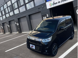 盛岡支店のスタイリッシュなガレージ前に停車する、黒（ブルーイッシュブラックパール）のスズキ・ワゴンRスティングレイ。キリッとしたフロントマスクと専用アルミホイールが特徴の一台です