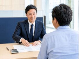 自社ローンの返済期間や月々の支払額について、資料と電卓を使いながら相談する中古車販売店スタッフと男性客。