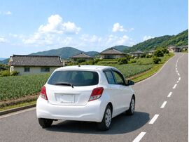 淡路島の坂道を走る白いコンパクトカー。カタログ燃費と実燃費の違いや坂道走行による燃費への影響をイメージした写真。
