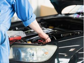 中古車のエンジンルームを点検する整備士。整備記録簿や点検・部品交換履歴を確認して、車の状態を見極めるイメージ。