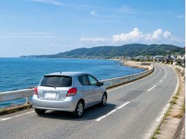 淡路島の海沿いを走るコンパクトカー。淡路島での車検や整備、信頼できる車検業者選びをイメージした写真。