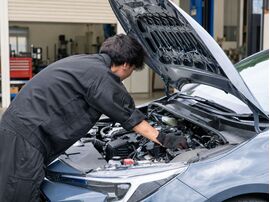 中古コンパクトカーのボンネットを開け、整備士がエンジンルームの状態を点検している様子