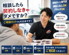 明るい中古車販売店の相談スペースで男性スタッフがお客様に寄り添いながら車購入や無料査定について丁寧に説明しているリアルな相談シーン
