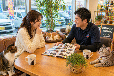 明るく開放的な店舗内で女性客がスタッフと車の購入や売却についてリラックスして相談している自然な商談風景とテーブルや周囲でくつろぐ猫たち