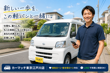 スマートフォンを手に笑顔で軽バンの前に立つ男性。 自社ローンで軽バンを購入した江戸川区在住の 個人事業主のイメージ。