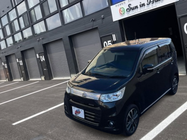 盛岡支店のスタイリッシュなガレージ前に停車する、黒（ブルーイッシュブラックパール）のスズキ・ワゴンRスティングレイ。キリッとしたフロントマスクと専用アルミホイールが特徴の一台です