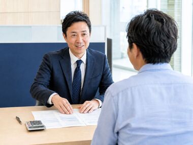 自社ローンの返済期間や月々の支払額について、資料と電卓を使いながら相談する中古車販売店スタッフと男性客。